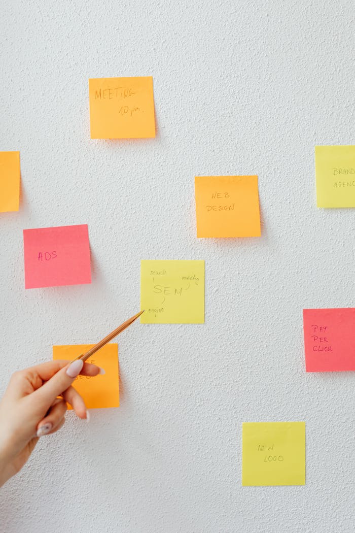 A hand pointing to vibrant sticky notes arranged on a white wall, highlighting planning and organization.
